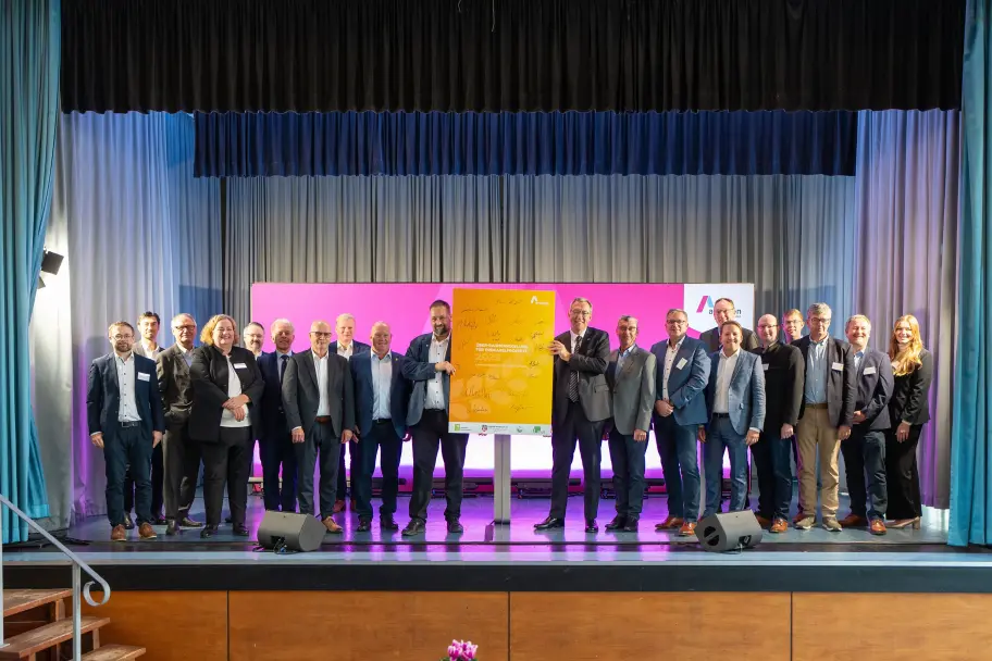 Gruppenbild von rund 20 Personen auf einer Bühne, die gemeinsam ein gelbes Plakat mit zahlreichen Unterschriften präsentieren. Das Plakat trägt die Aufschrift „Über-Rahmenregelung für Erdkabelprojekte 2025“. Dahinter eine pinkfarbene Wand mit dem Amprion-Logo.